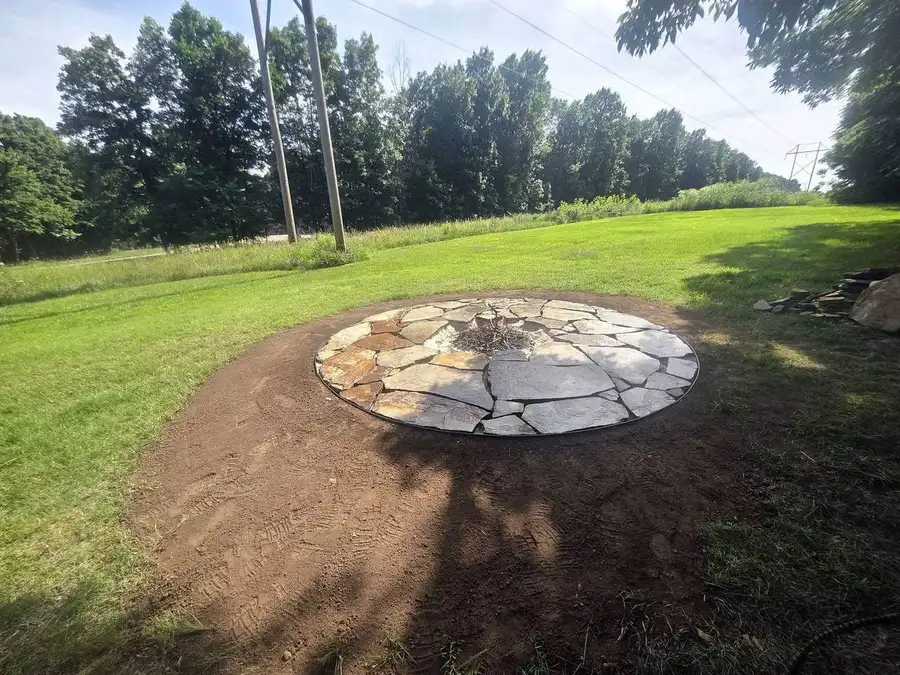 Flagstone fire pit patio in an open back lawn with fresh soil around it