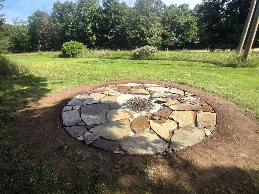 Flagstone fire pit in an open lawn with a tree line behind