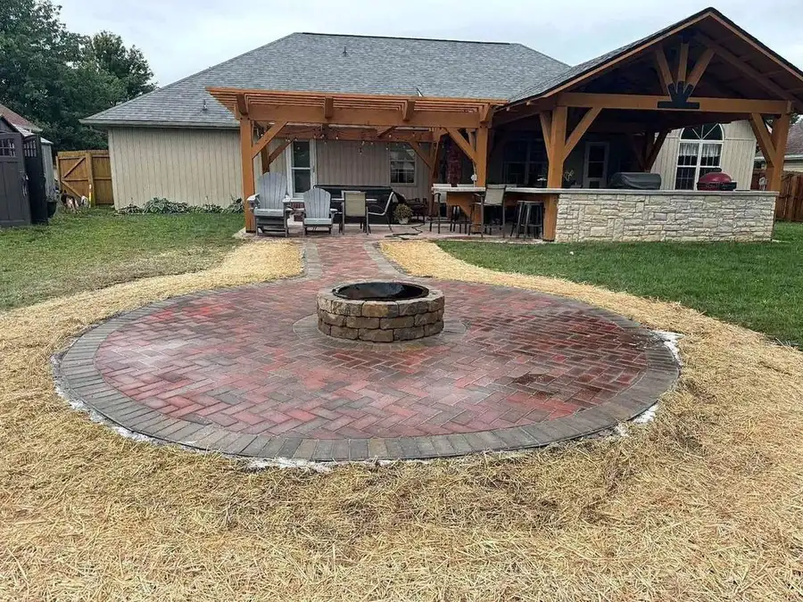 Brick paver patio with a round fire pit, curved border and mulch, behind a covered pavilion