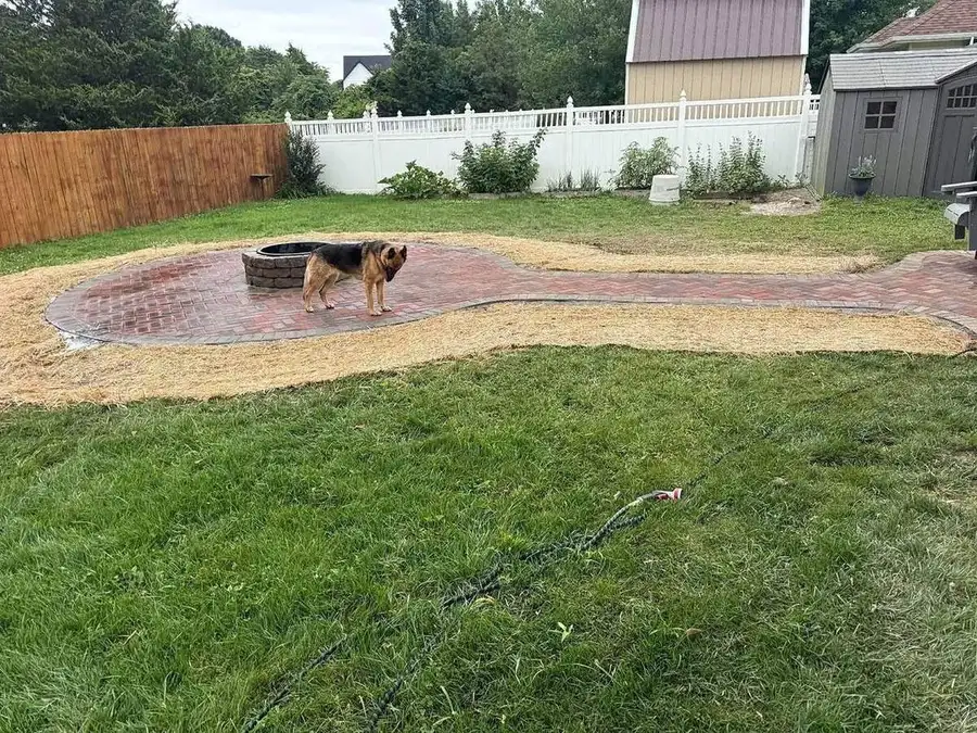 Brick paver patio curving out from a fire pit toward a lawn